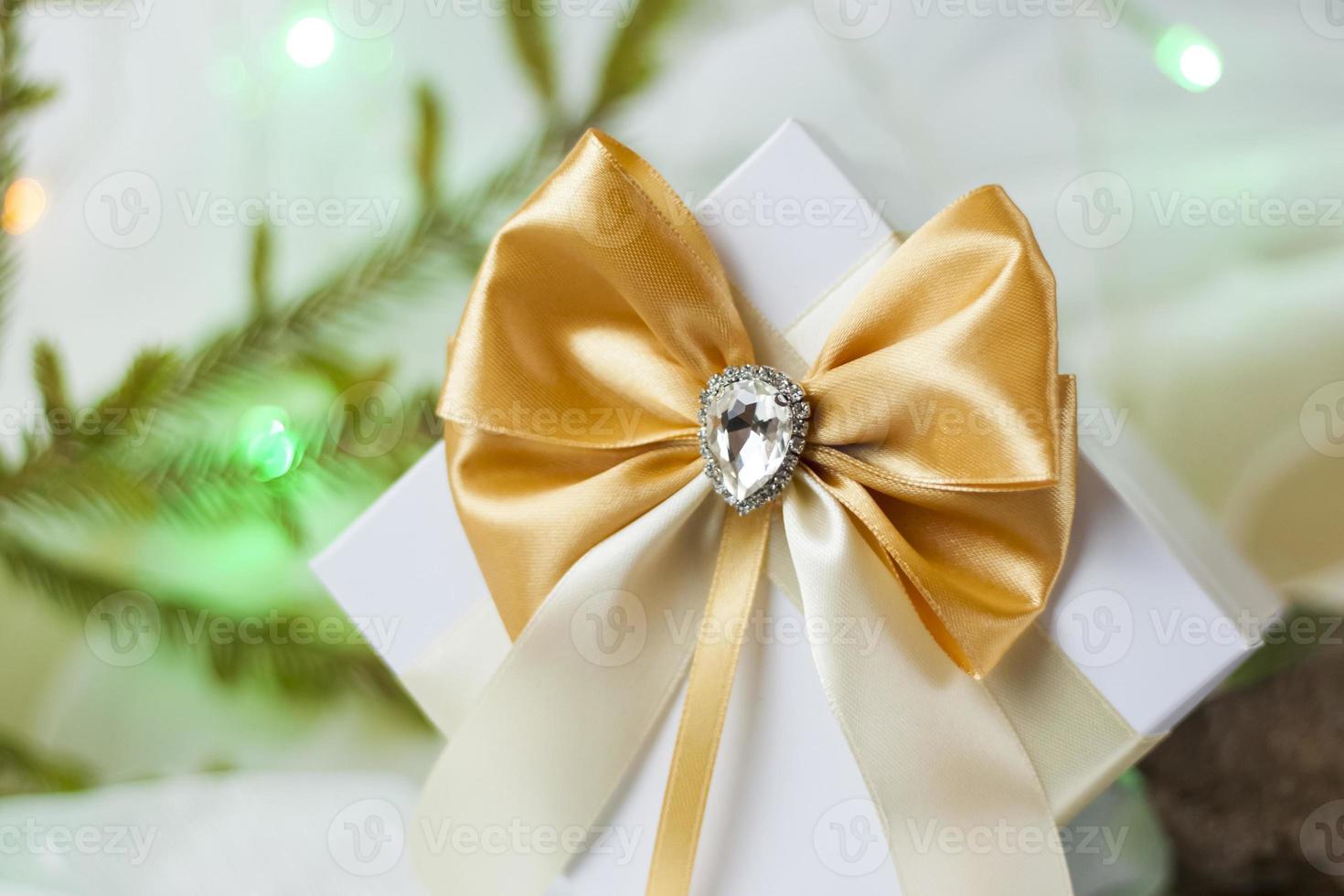 A Christmas gift decorated with a beautiful bow on a light background with a twig, if. Selective focus. the concept of Christmas and New Year. photo