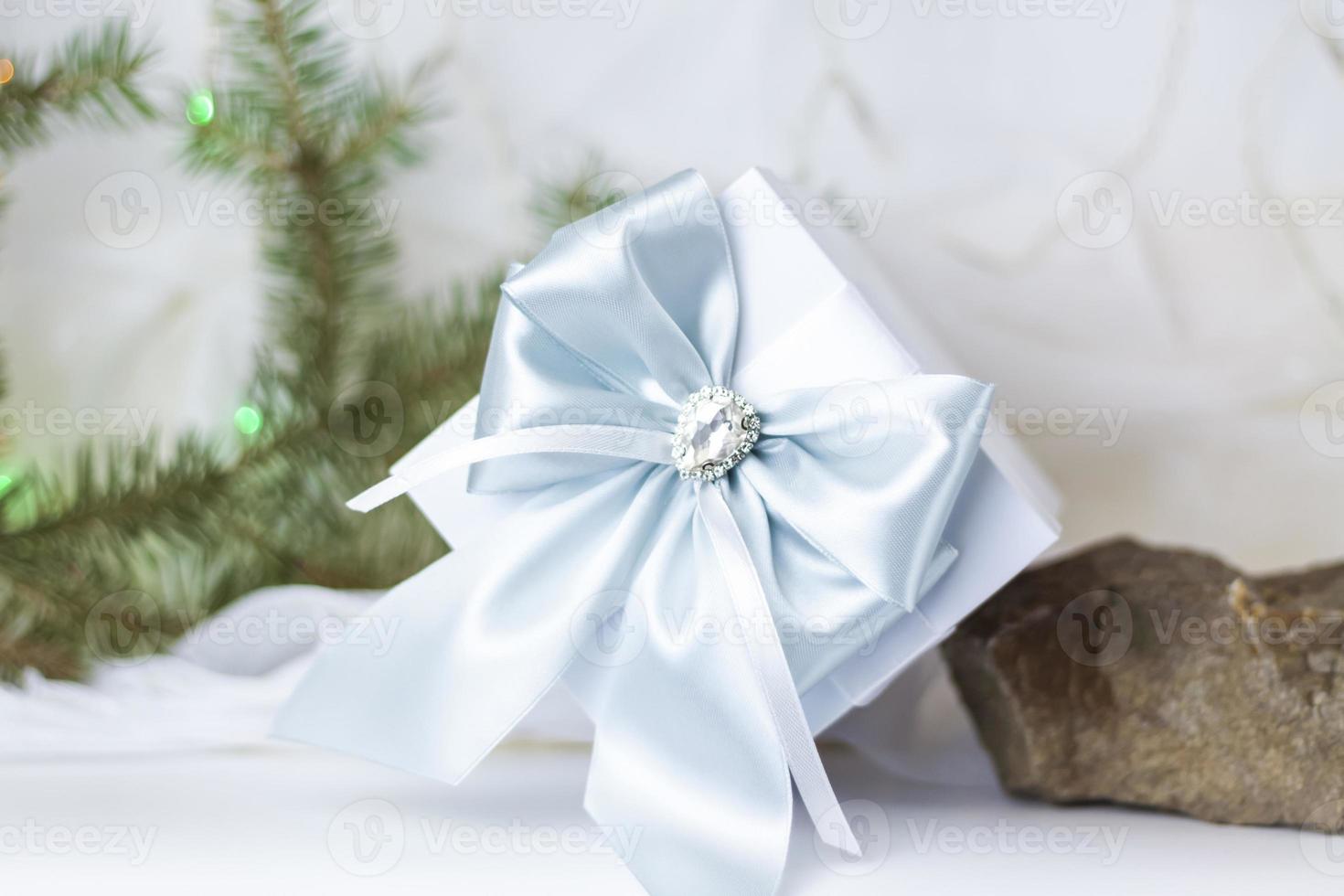 un regalo de navidad decorado con un hermoso lazo sobre un fondo claro con una ramita de abeto. regalos, alegría, sorpresa. enfoque selectivo. el concepto de navidad y año nuevo. foto