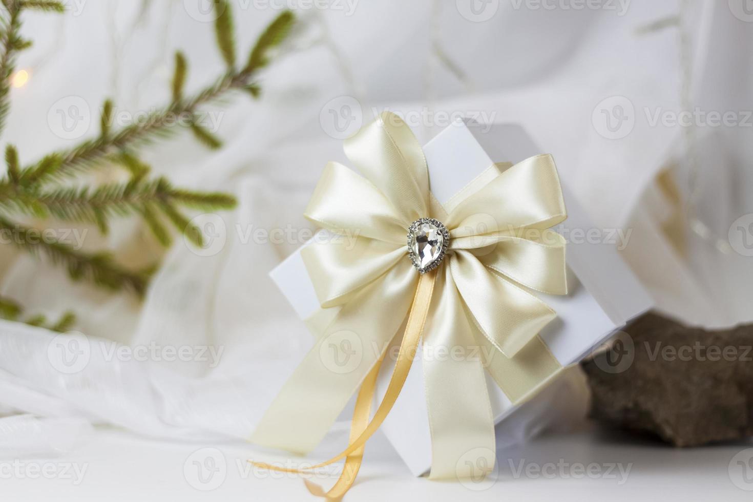 A Christmas gift decorated with a beautiful bow on a light background with a twig, if. Selective focus. the concept of Christmas and New Year. photo