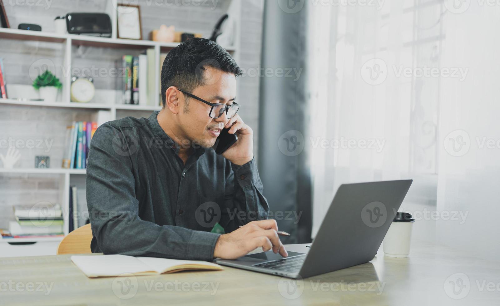 Freelance business man calling on mobile smartphone while working with laptop on table, businessman mobile phone to calling with customers or shopping online. Smart phone conversation conferrence. photo