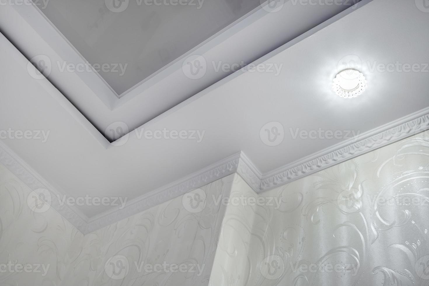 Detail of corner ceiling with intricate crown molding. Suspended ceiling and drywall construction in empty room in apartment or house. Stretch ceiling white and complex shape. photo