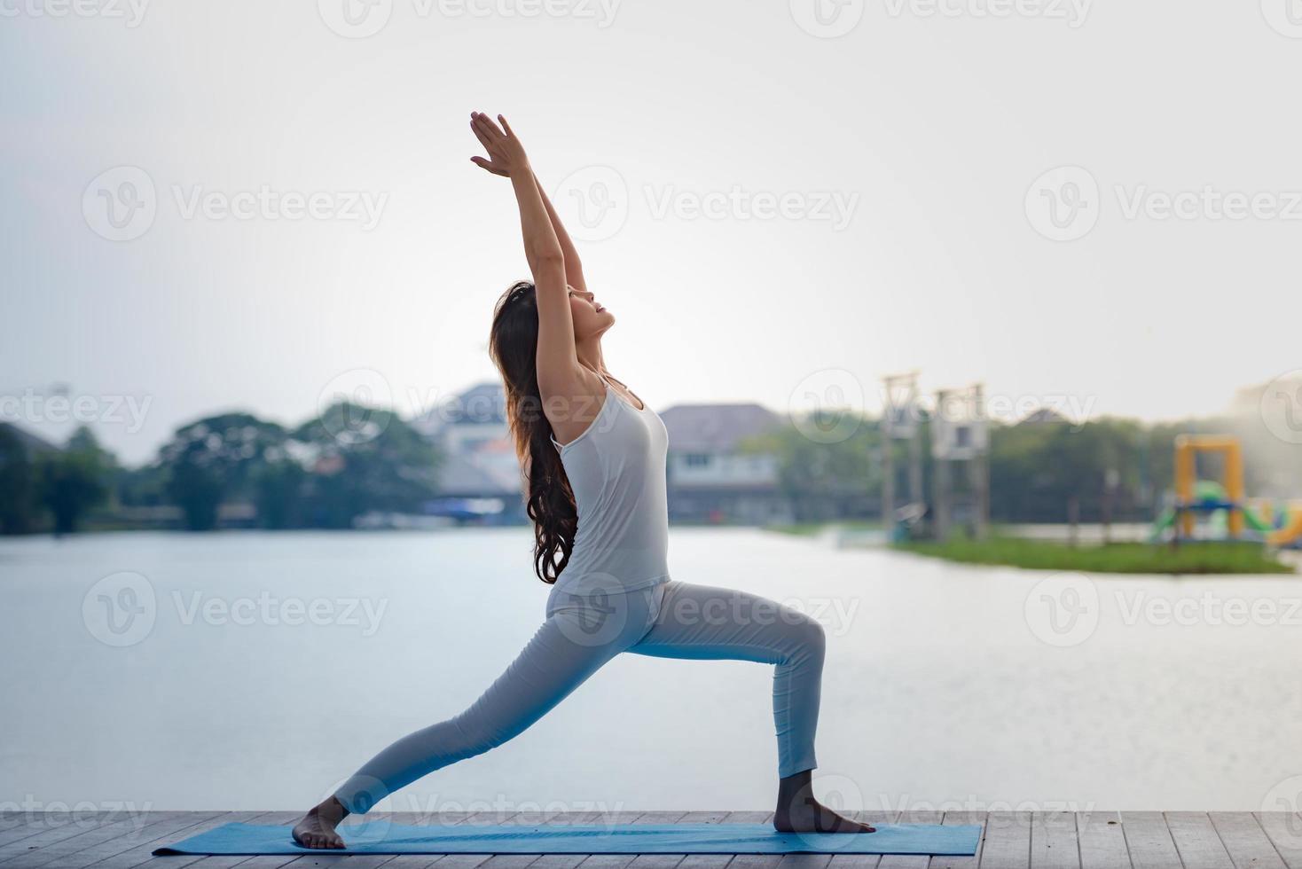 Young Asian healthy woman doing yoga in the park at lake pier. photo