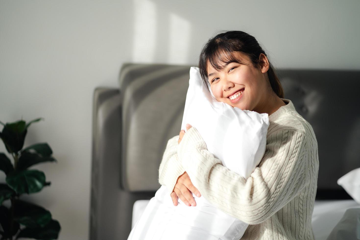 Smiling woman embracing pillow on bed at home photo
