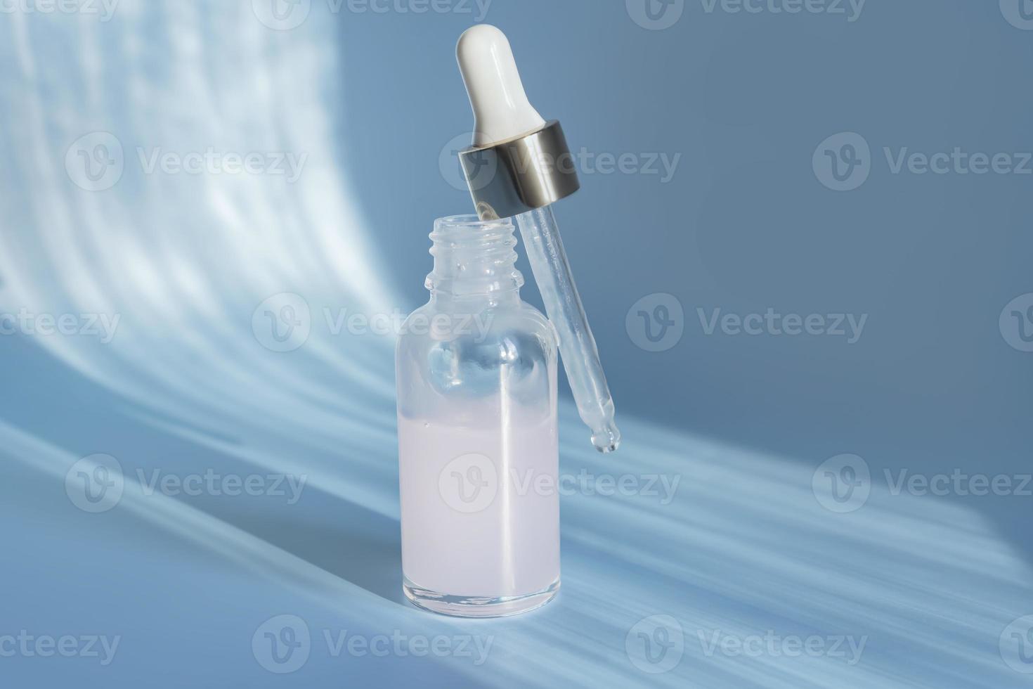 Glass cosmetic bottle dropper with beuty oil or serum for skin care on blue background. Natural skin care concept. Hard shadows photo