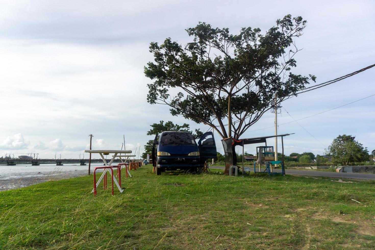 concepto de cafetería móvil. silla y mesa frente a la autocaravana. concepto de picnic. autocaravana estacionada debajo del árbol y al lado del río. foto