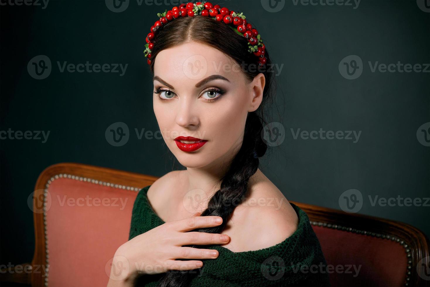 portrait of smiling young beautiful brunette with red wreath and braid on dark background photo