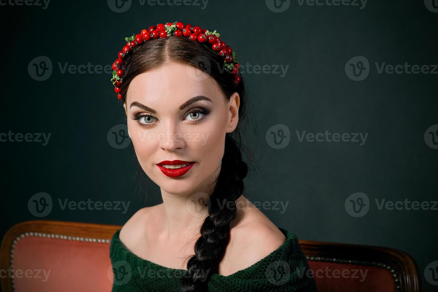 portrait of smiling young beautiful brunette with red wreath and braid on dark background photo