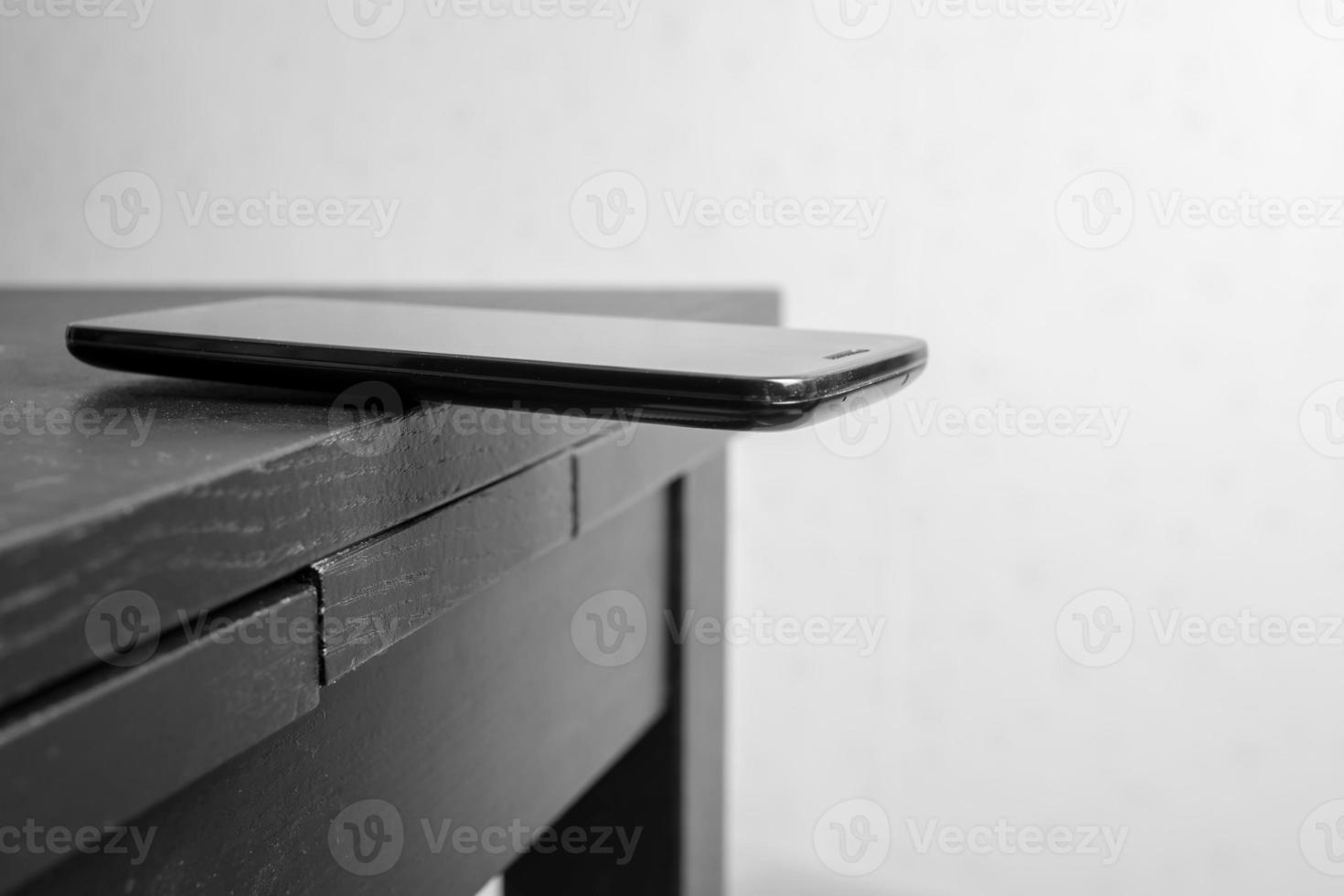 Smartphone is lying on the edge of the table, carelessly left with the possibility of falling. photo