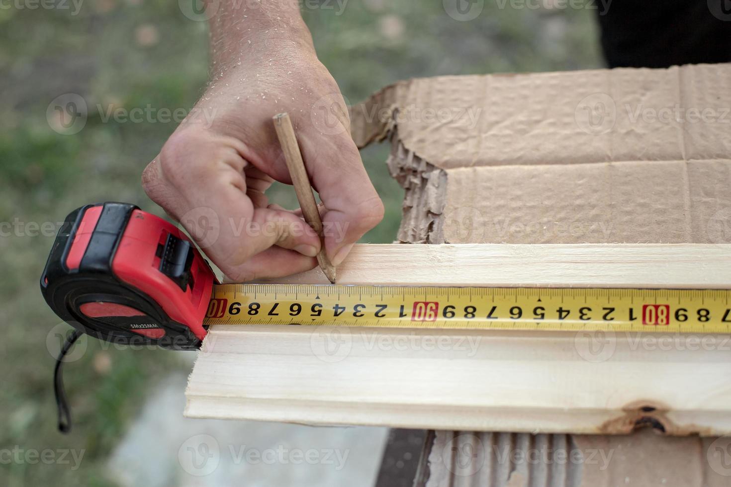 Carpenter hands measure with a tape measure on a wooden board and mark the required length with a pencil. photo
