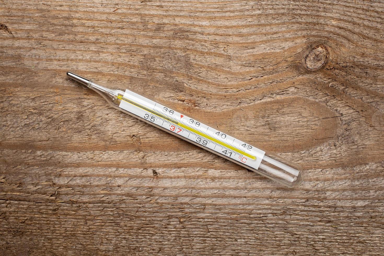 Medical mercury thermometer with a temperature of 37 degrees on a wooden texture. Top view. photo