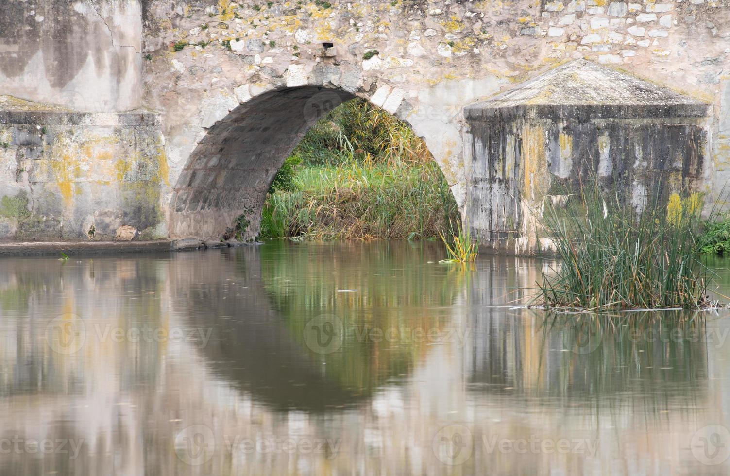 Close-up and detail shot of the arch of an old stone bridge. The bridge is reflected in the calm water of a river. photo