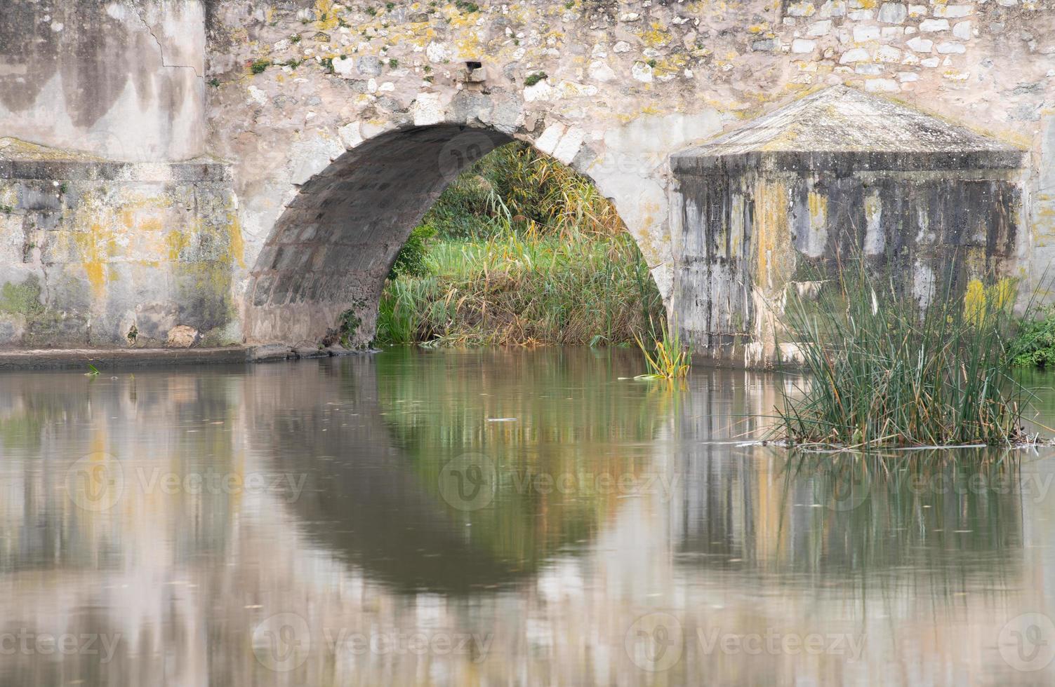 toma de primer plano y detalle del arco de un antiguo puente de piedra. el puente se refleja en las tranquilas aguas de un río. foto