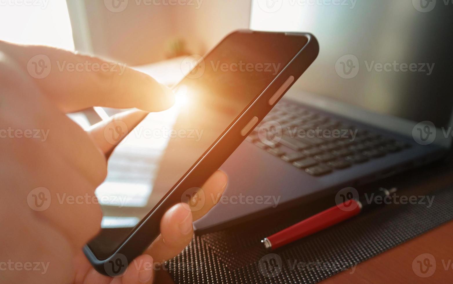 mano que señala el teléfono inteligente sobre una computadora portátil borrosa foto