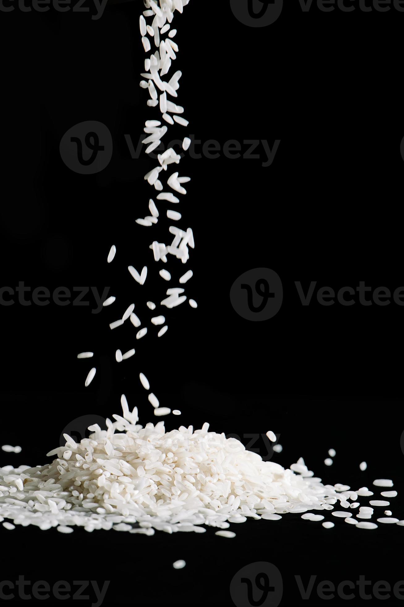 Raw white rice is falling on table. Pile of uncooked long rice on black