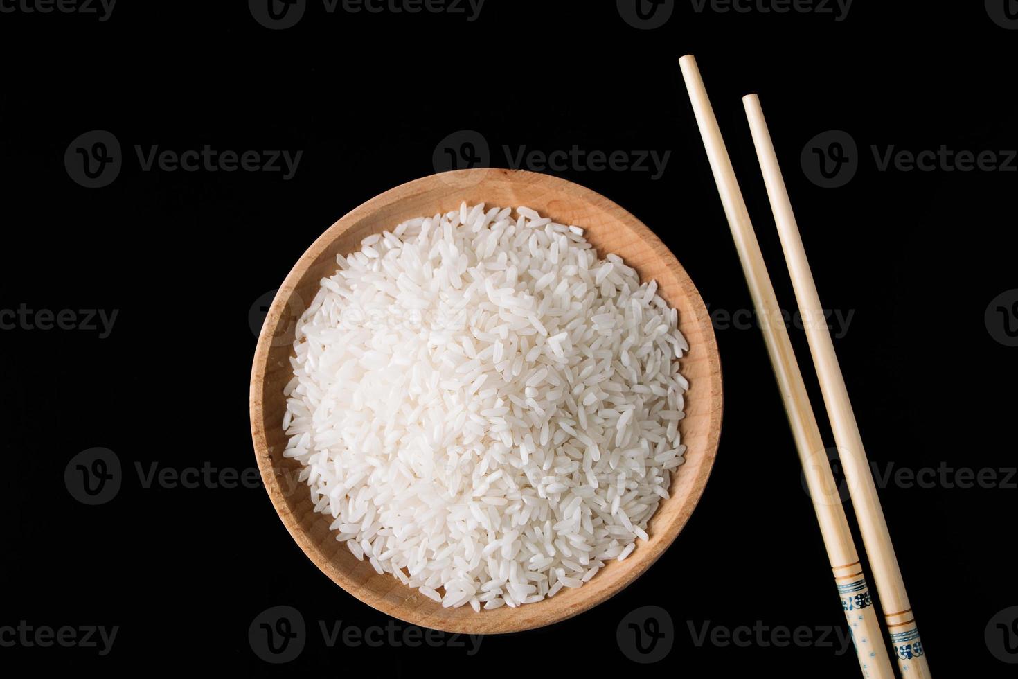 Raw white rice and chopsticks on black background. Long uncooked rice in wooden plate. photo