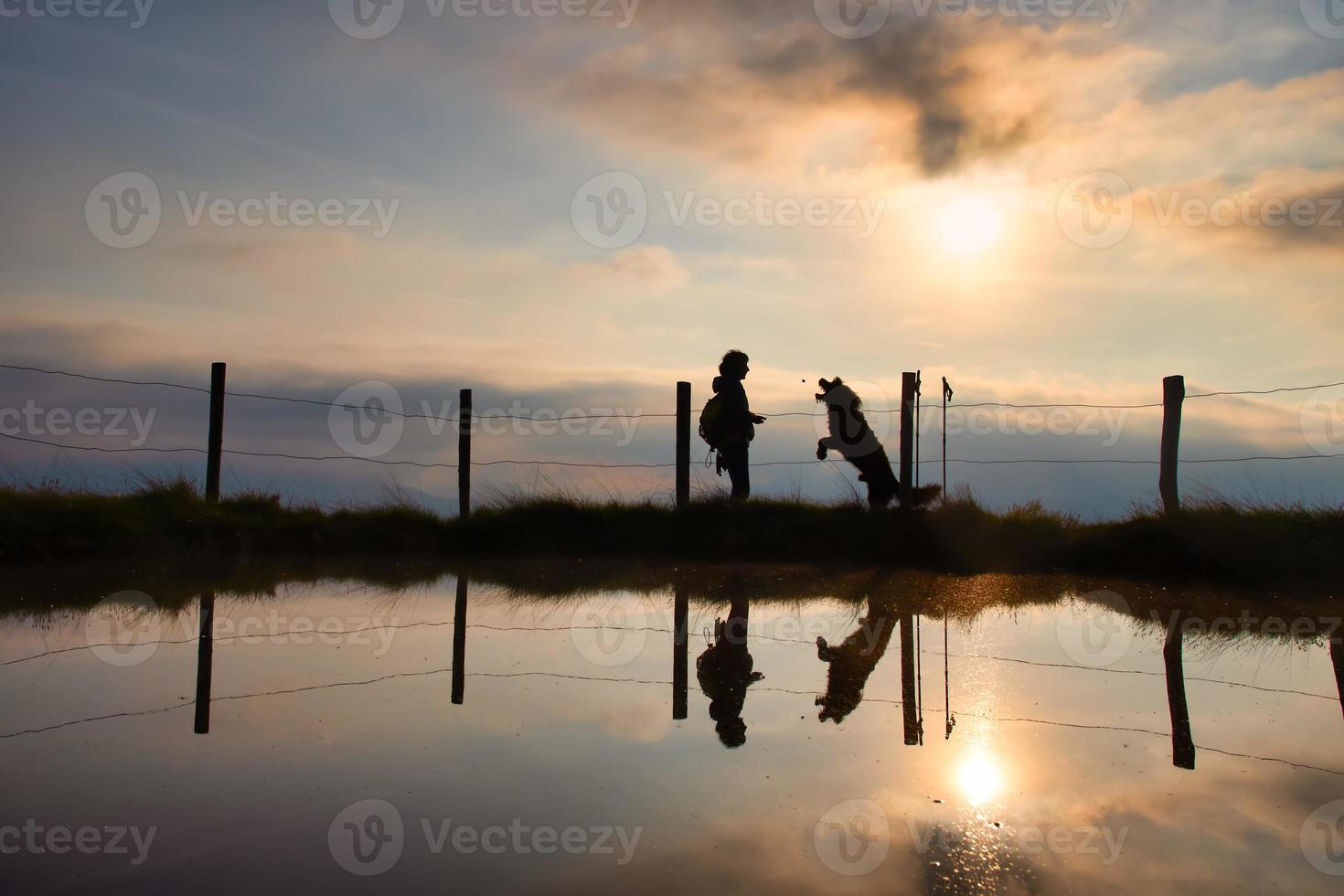 A woman gives a cookie to her dog during a walk in the mountains at sunset photo