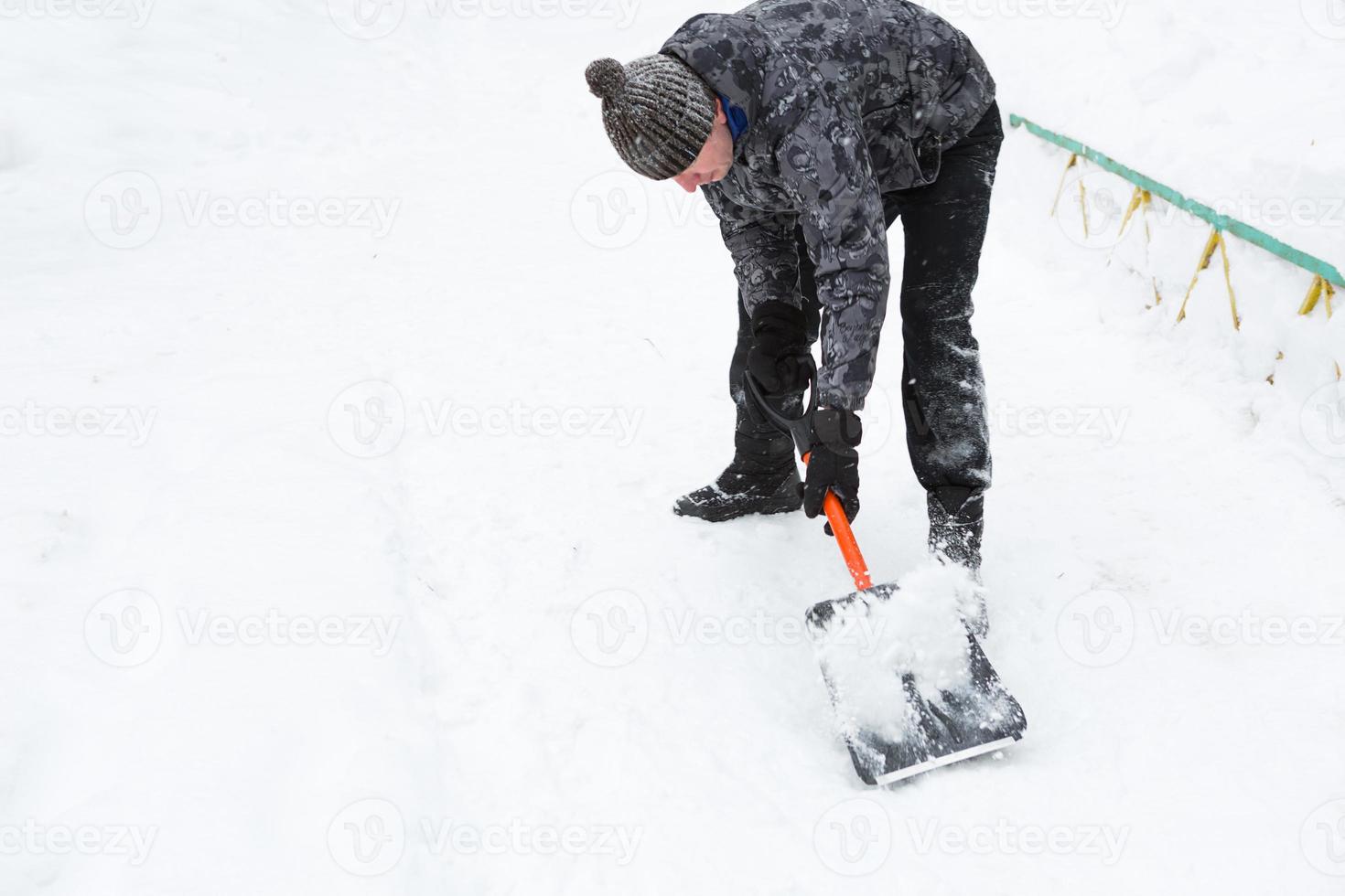 A man cleans snow with a shovel in winter in a swept yard after a snowfall. Winter weather conditions, snow shovel for car trunk photo