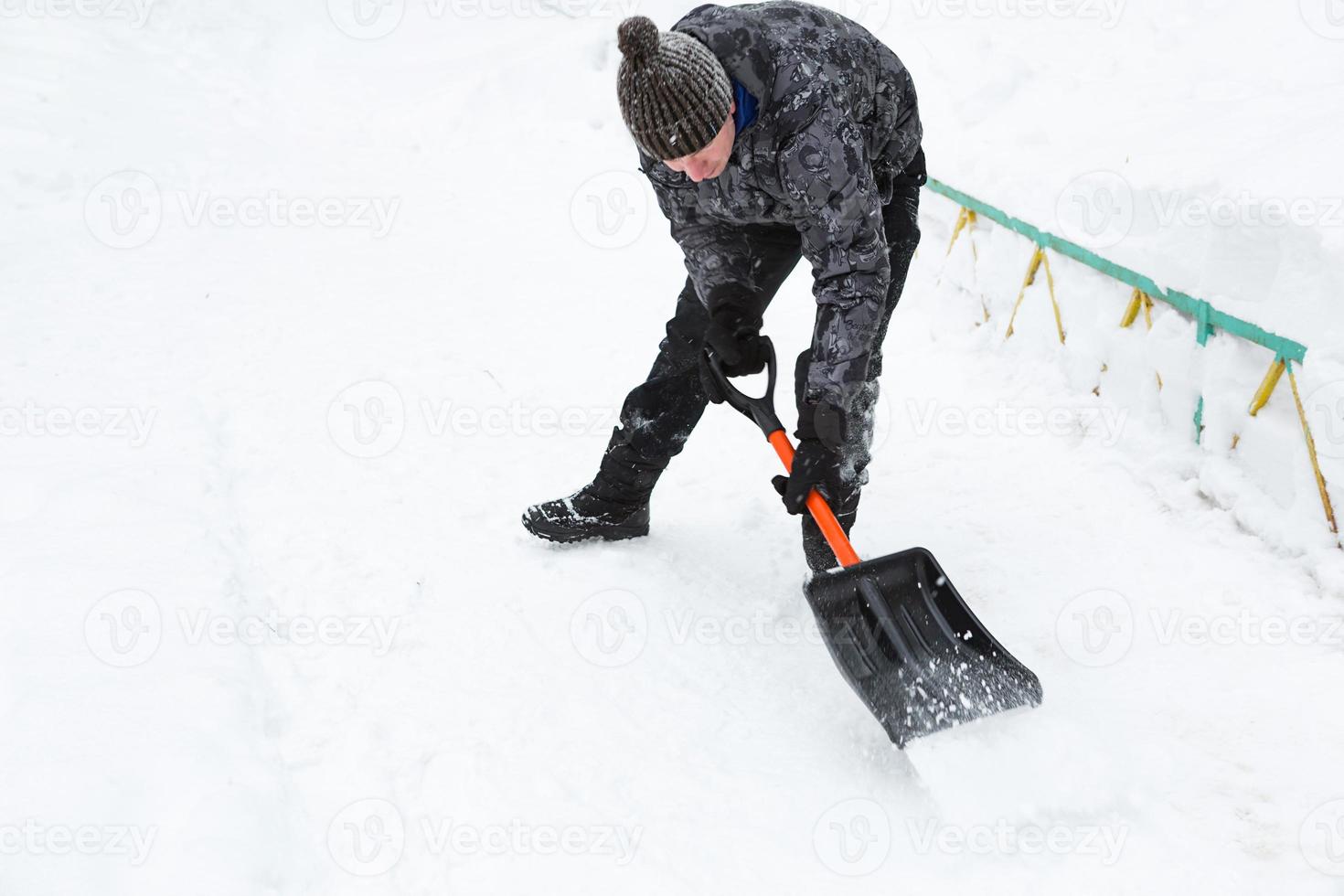 A man cleans snow with a shovel in winter in a swept yard after a snowfall. Winter weather conditions, snow shovel for car trunk photo