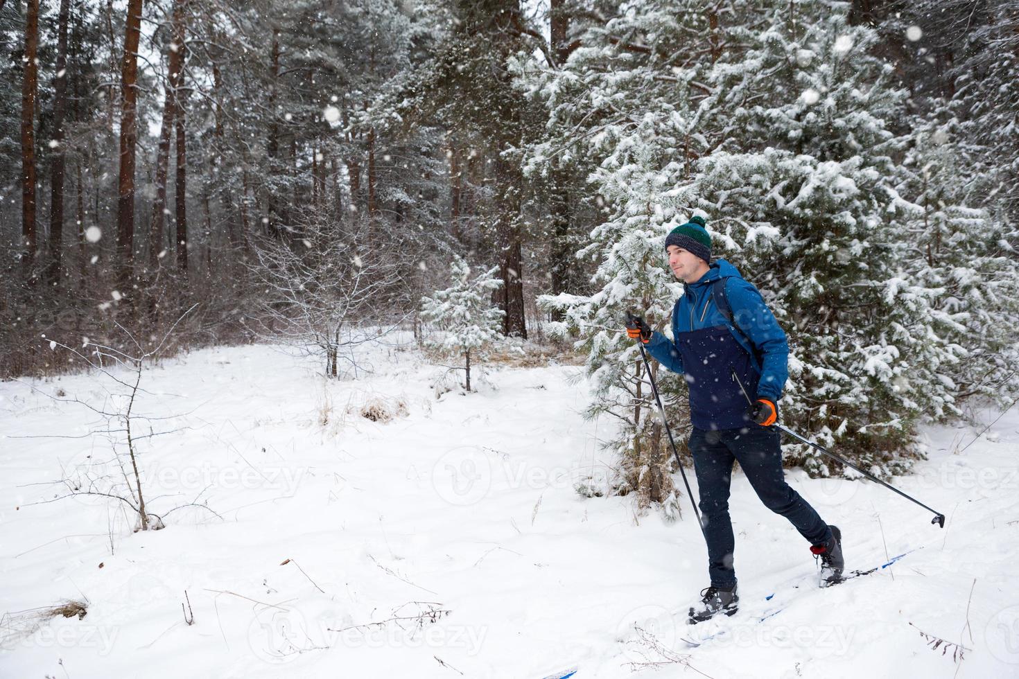 esquiador con mochila y sombrero con pompón con bastones de esquí en las manos sobre el fondo de un bosque nevado. esquí de fondo en bosque de invierno, deportes al aire libre, estilo de vida saludable, turismo de deportes de invierno. foto