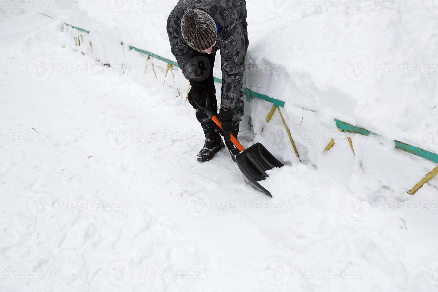 A man cleans snow with a shovel in winter in a swept yard after a snowfall. Winter weather conditions, snow shovel for car trunk photo