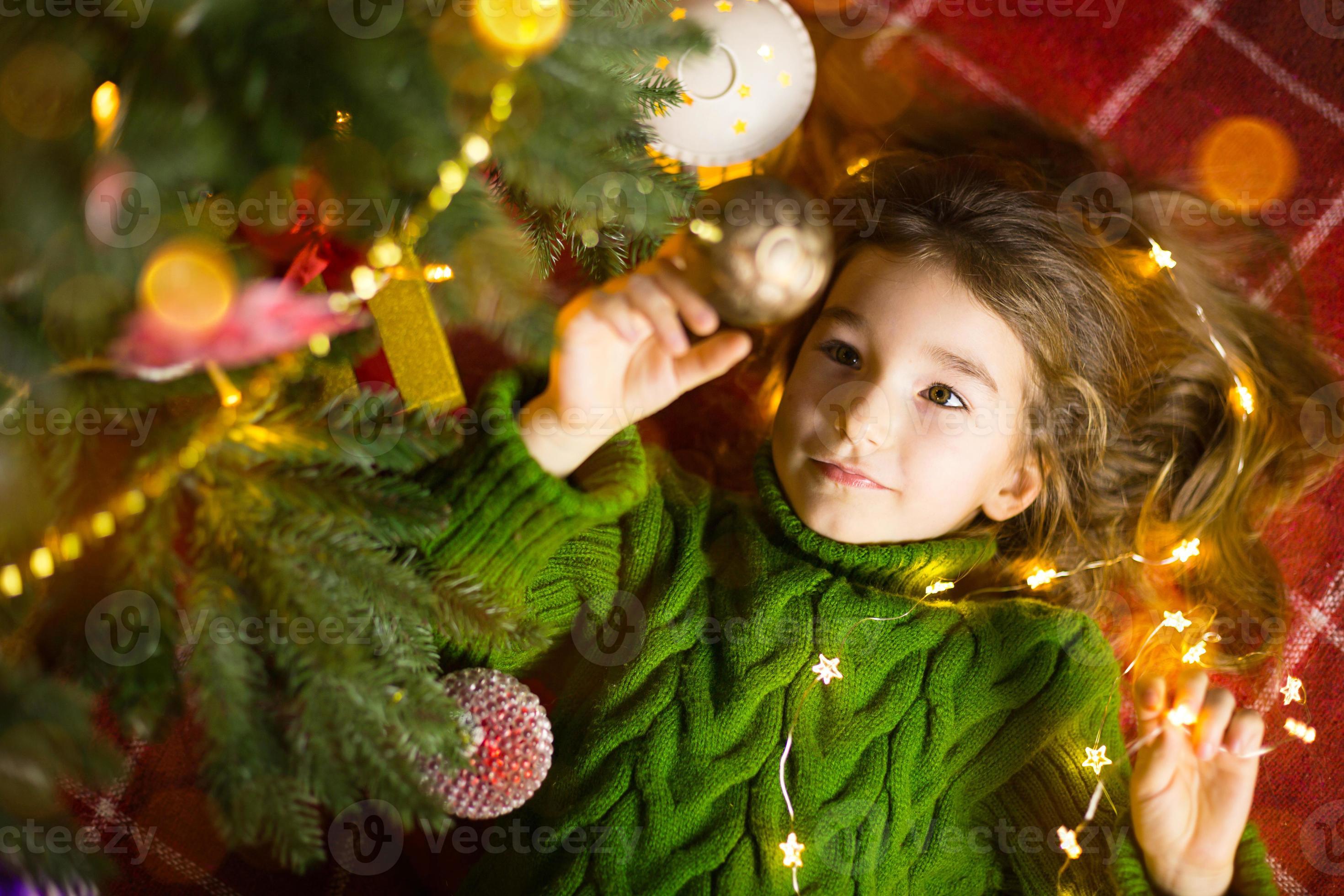A girl with long hair and garlands lies on a red plaid under a Christmas  tree with toys in a warm knitted sweater. Christmas, New Year, children's  emotions, joy, expectation of a miracle and gifts 14335935 Stock Photo at  Vecteezy