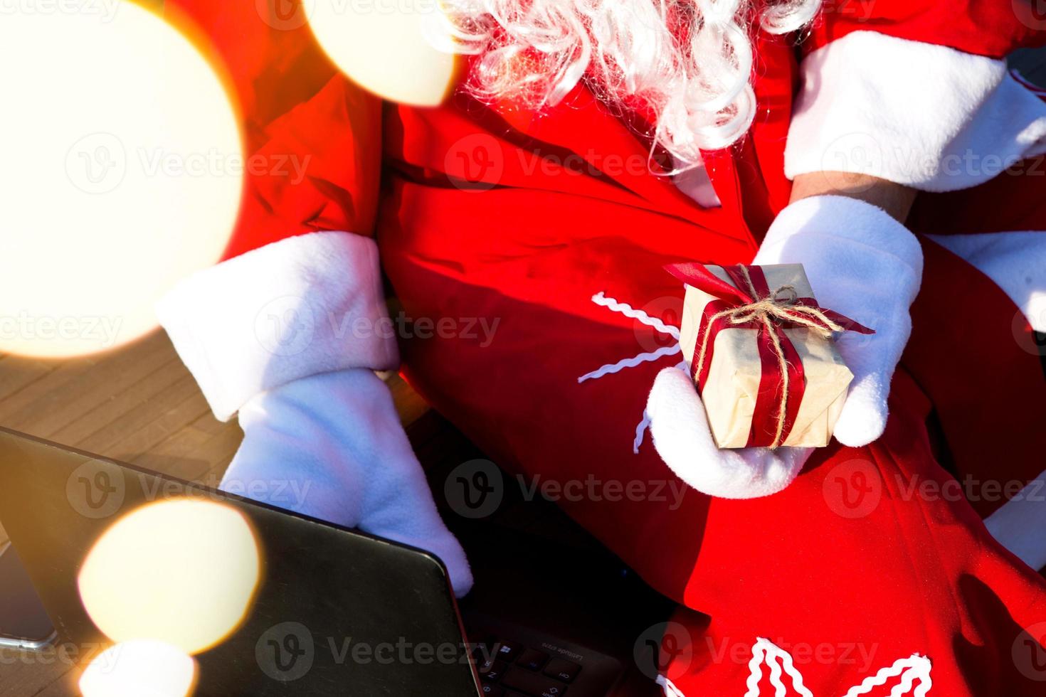Santa Claus with a laptop and a gift in his hand. Order gifts for Christmas and new year through the online store. Booking the services of an animator for the holidays. photo