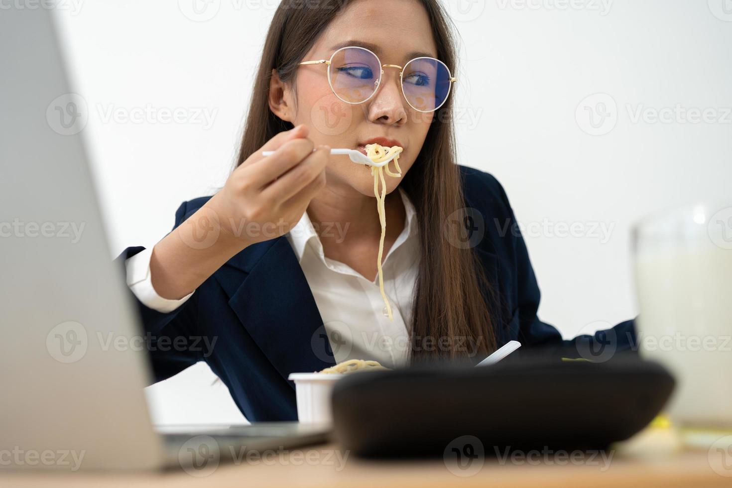 Busy and tired businesswoman eating spaghetti for lunch at the Desk office and working to deliver financial statements to a boss. Overworked and unhealthy for ready meals, burnout concept. photo
