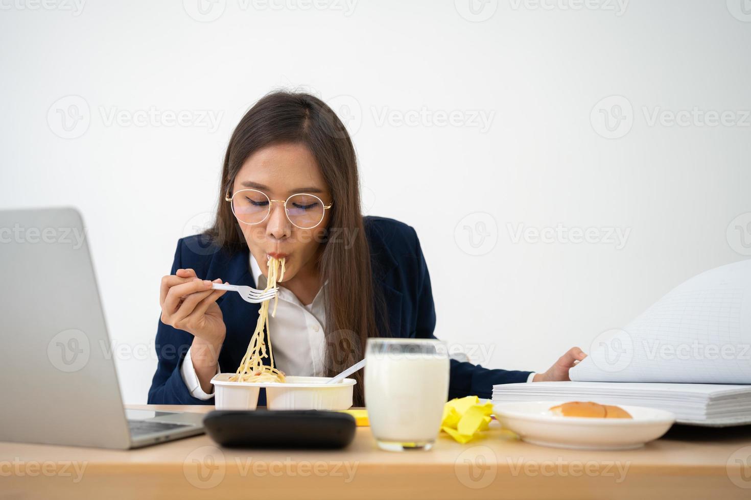 Busy and tired businesswoman eating spaghetti for lunch at the Desk office and working to deliver financial statements to a boss. Overworked and unhealthy for ready meals, burnout concept. photo