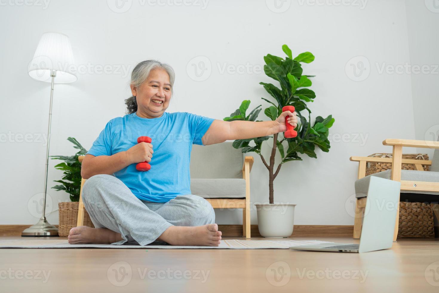 Asian senior woman lifting dumbbell for exercise and workout at home. Active mature woman doing stretching exercise in living room. Exercise Active and healthy for older, elder, and senior concept. photo