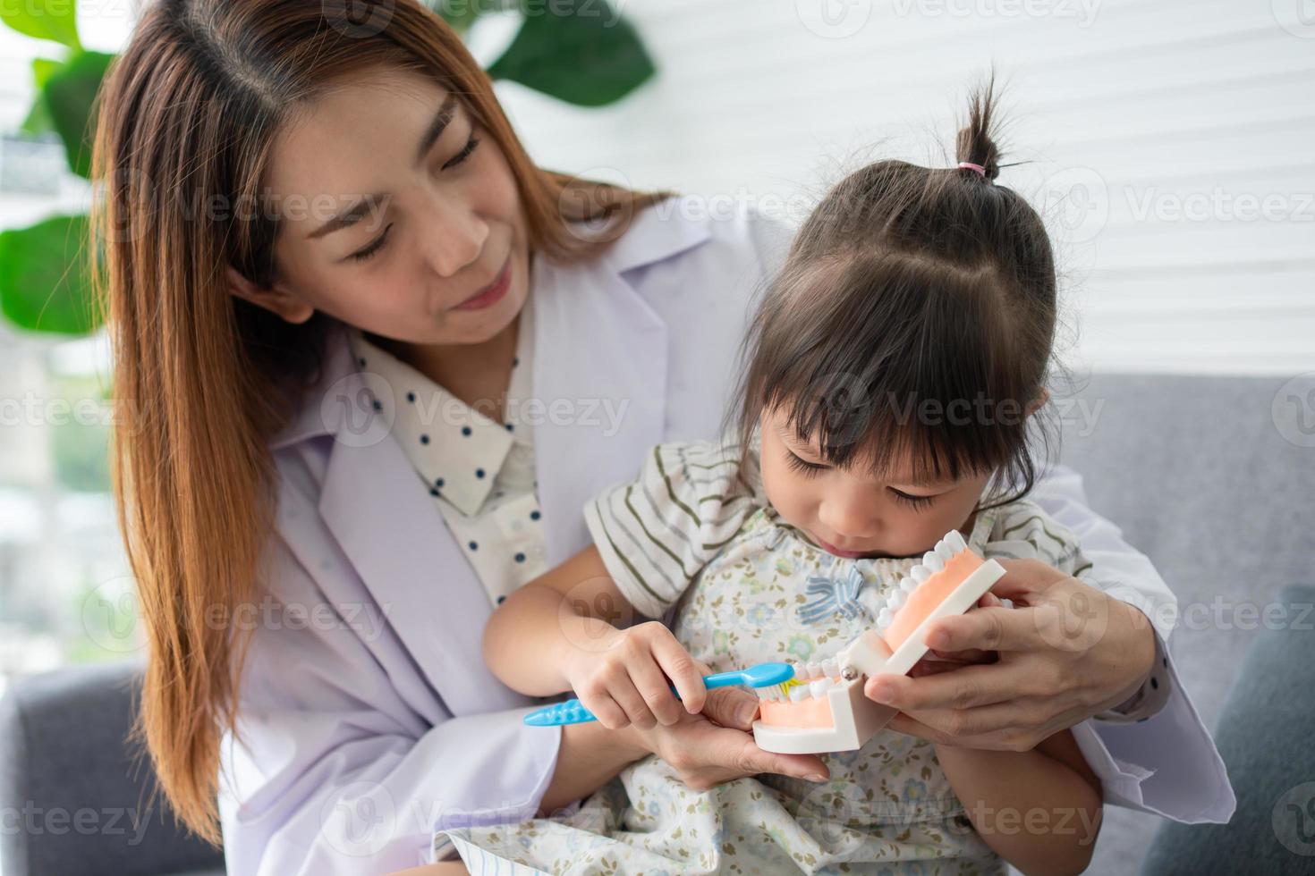 Asian female dentist teaching cute little girl brushing teeth with toothbrush and stomatologist telling girl child about oral hygiene in dental clinic, Education and prevention cavities concept. photo