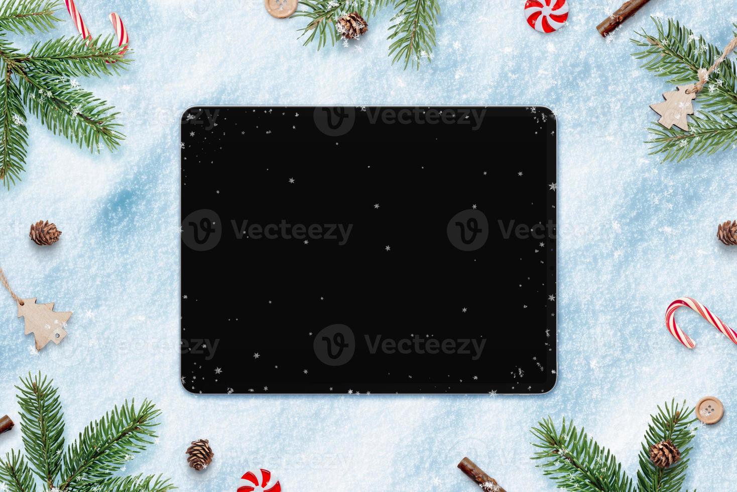 Tablet in snow for app design or copy promotion. Surrounded by Christmas decorations. Top view, flat lay photo