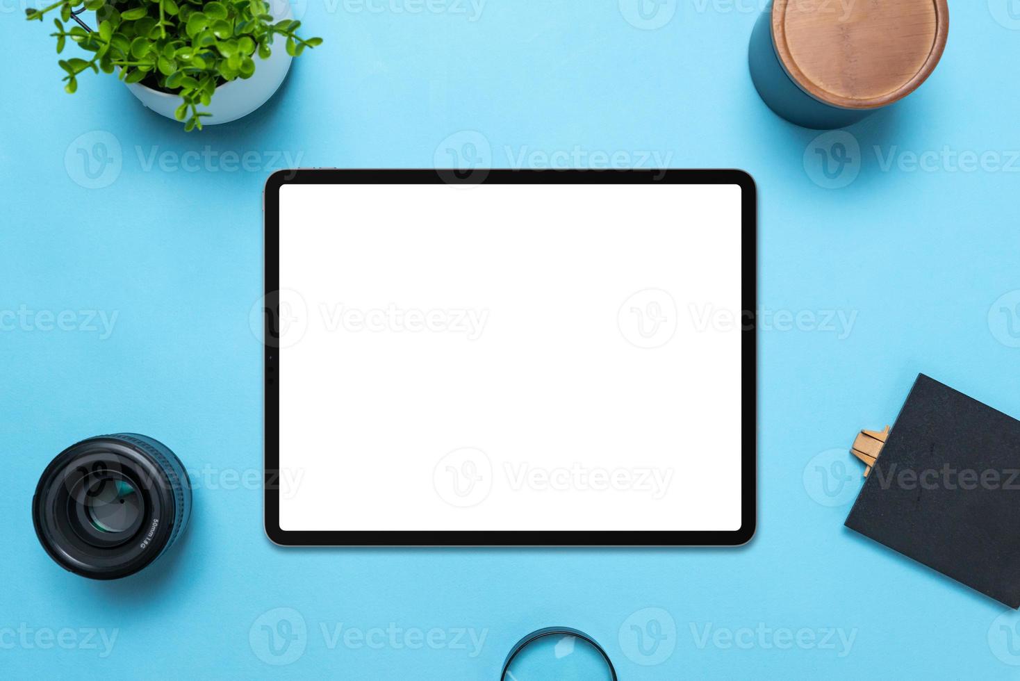 Tablet with isolated white display on blue table. Top view, flat lay composition. The plant, lens, box, magnifying glass and table beside photo