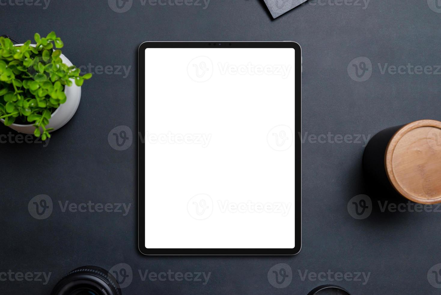 Tablet mockup on black table surrounded by objects. Isolated display in white for app or web design promotion. Top view, flat lay composition photo