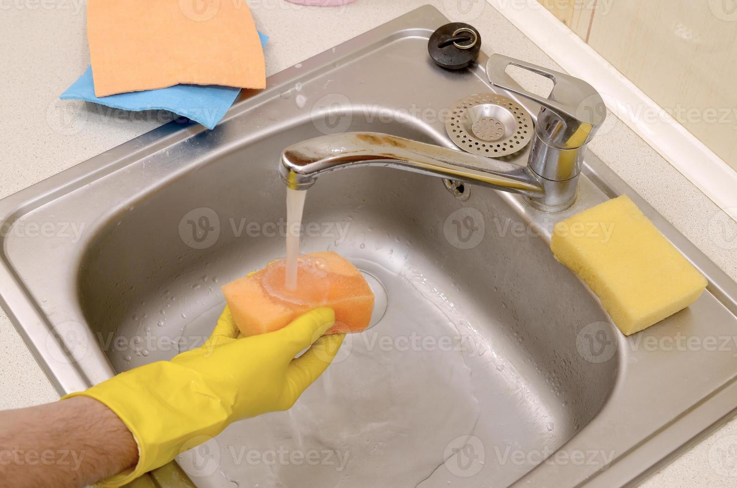 Person or householder cleaning the kitchen sink with sponge in close up view photo
