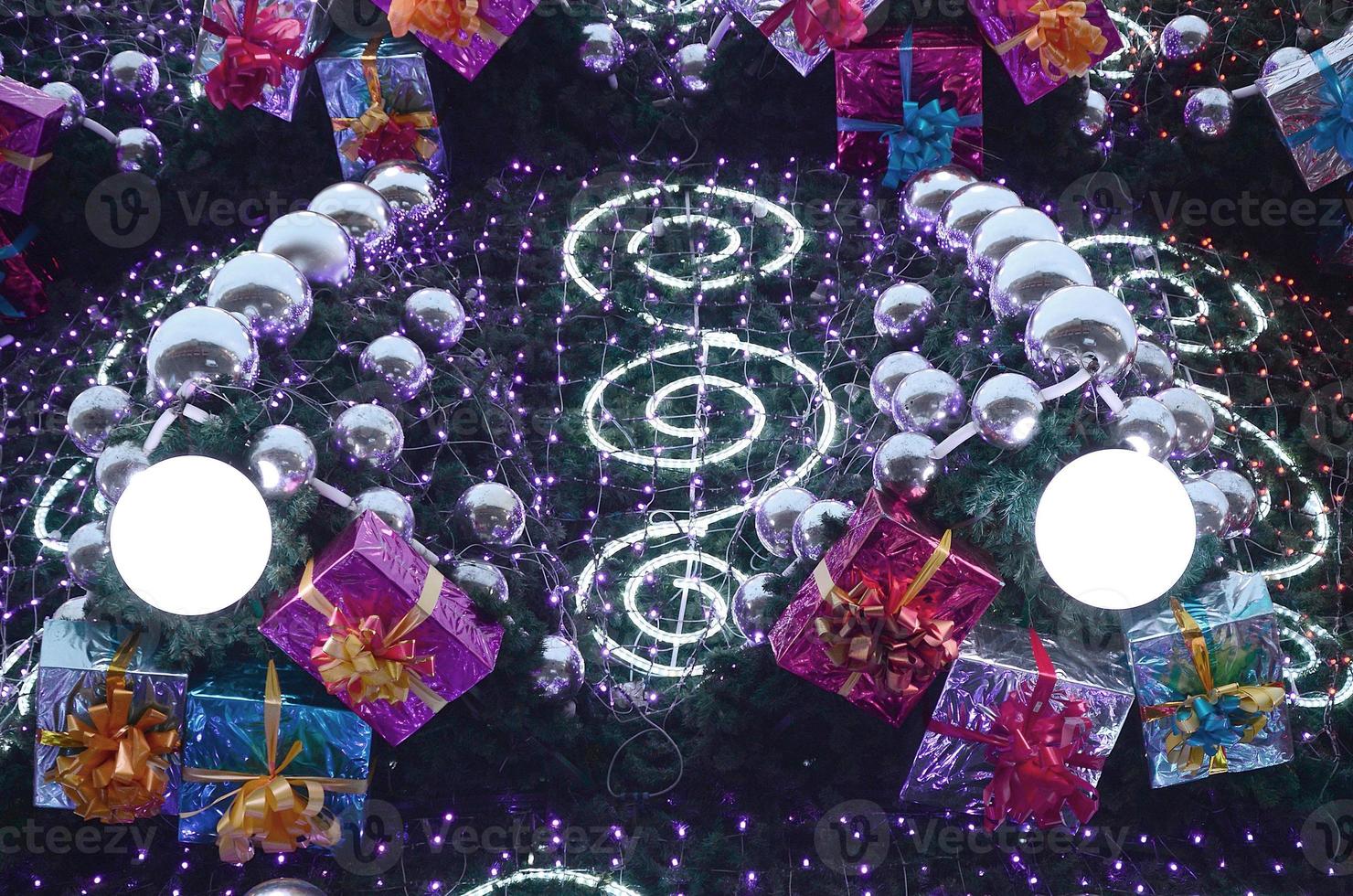A fragment of a huge Christmas tree with many ornaments, gift boxes and luminous lamps. Photo of a decorated Christmas tree close-up