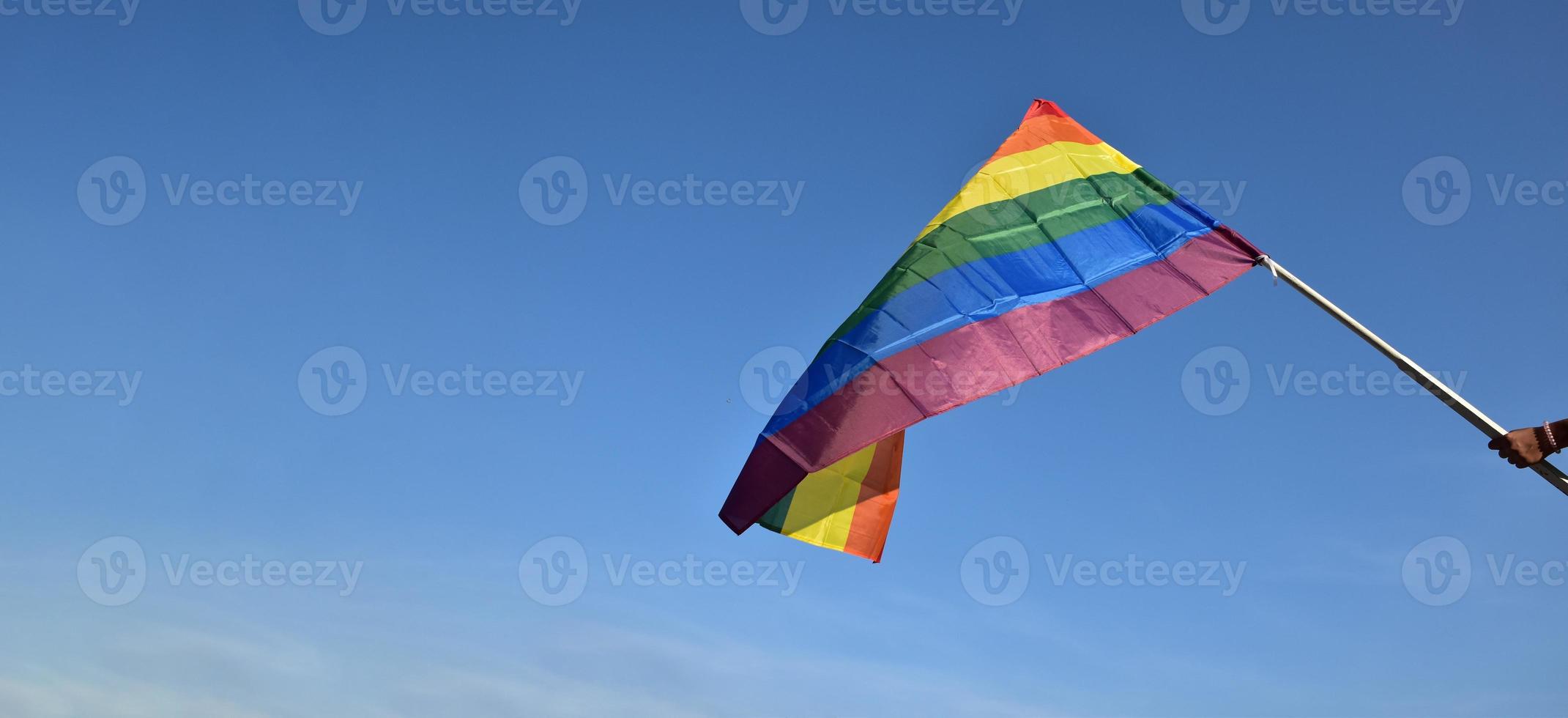 bandera del arco iris sosteniendo en la mano contra el fondo del cielo azul, concepto para la celebración lgbt en el mes del orgullo, junio, en todo el mundo. foto