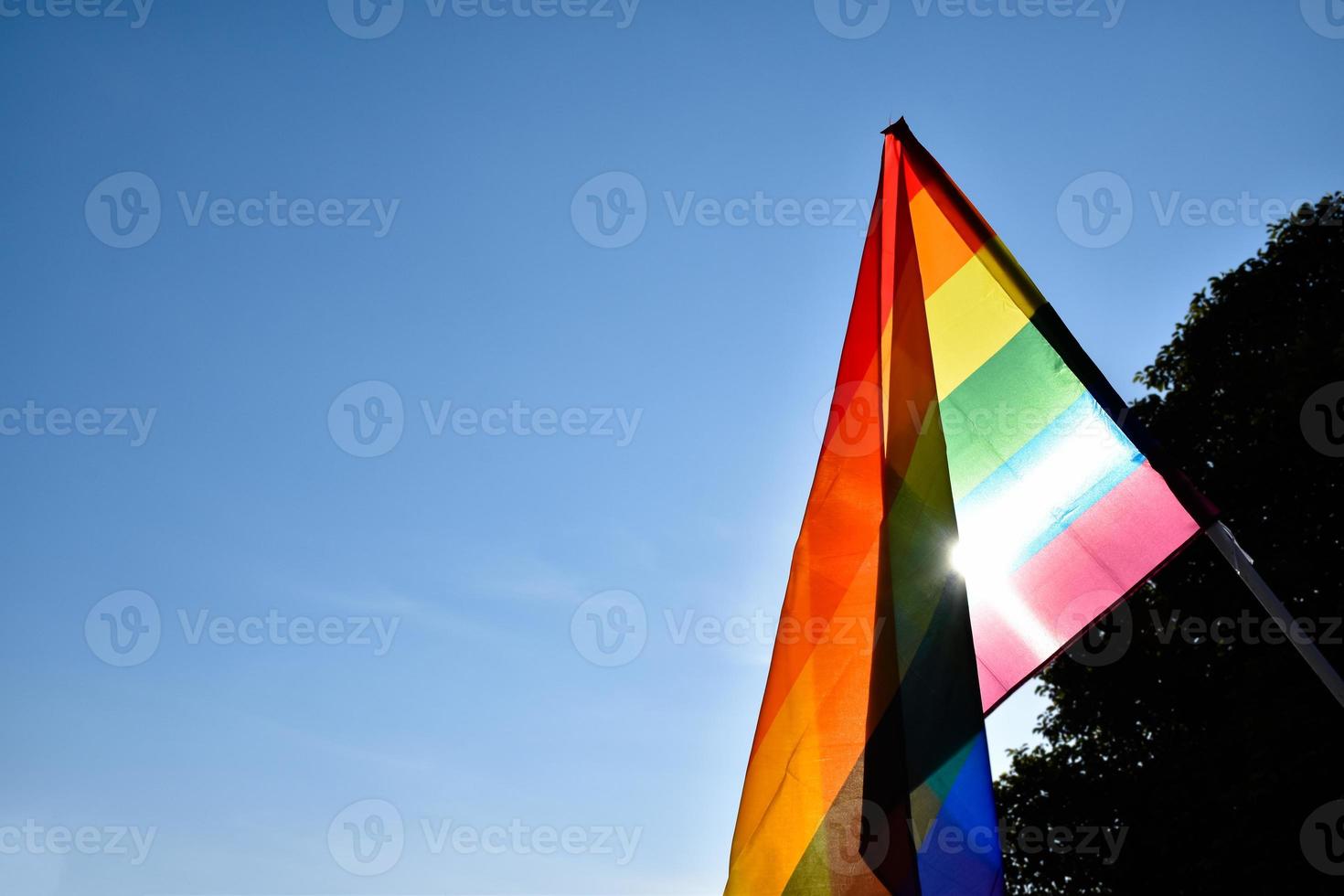 bandera del arco iris sosteniendo en la mano contra el fondo del cielo azul, concepto para la celebración lgbt en el mes del orgullo, junio, en todo el mundo. foto