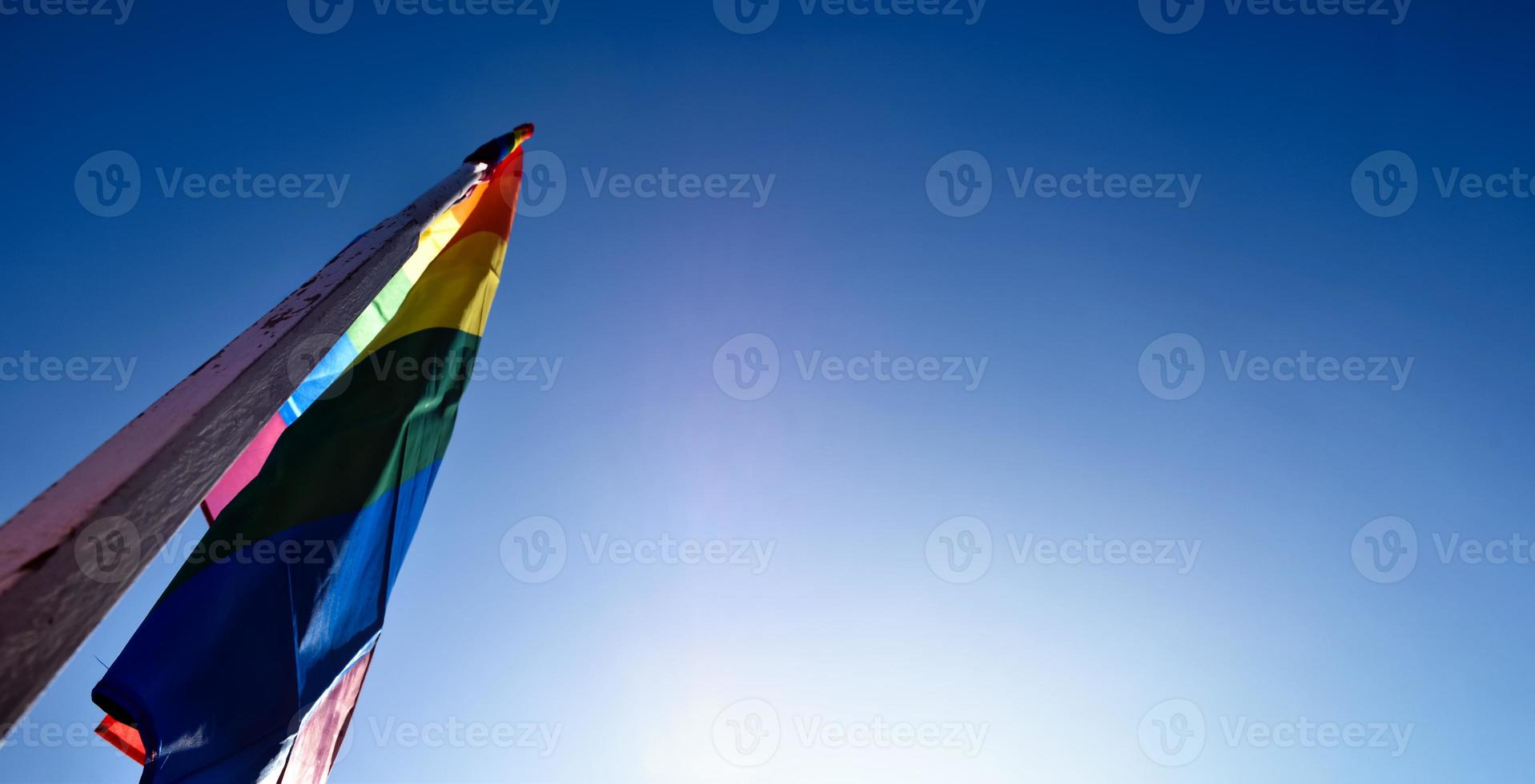 Look up view of rainbow flag, LGBT simbol, against clear bluesky background, soft and  selective focus, concept for LGBT celebration in pride month, June, around the world, copy space. photo