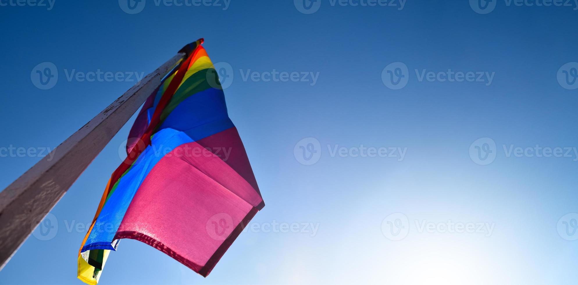 Look up view of rainbow flag, LGBT simbol, against clear bluesky background, soft and  selective focus, concept for LGBT celebration in pride month, June, around the world, copy space. photo