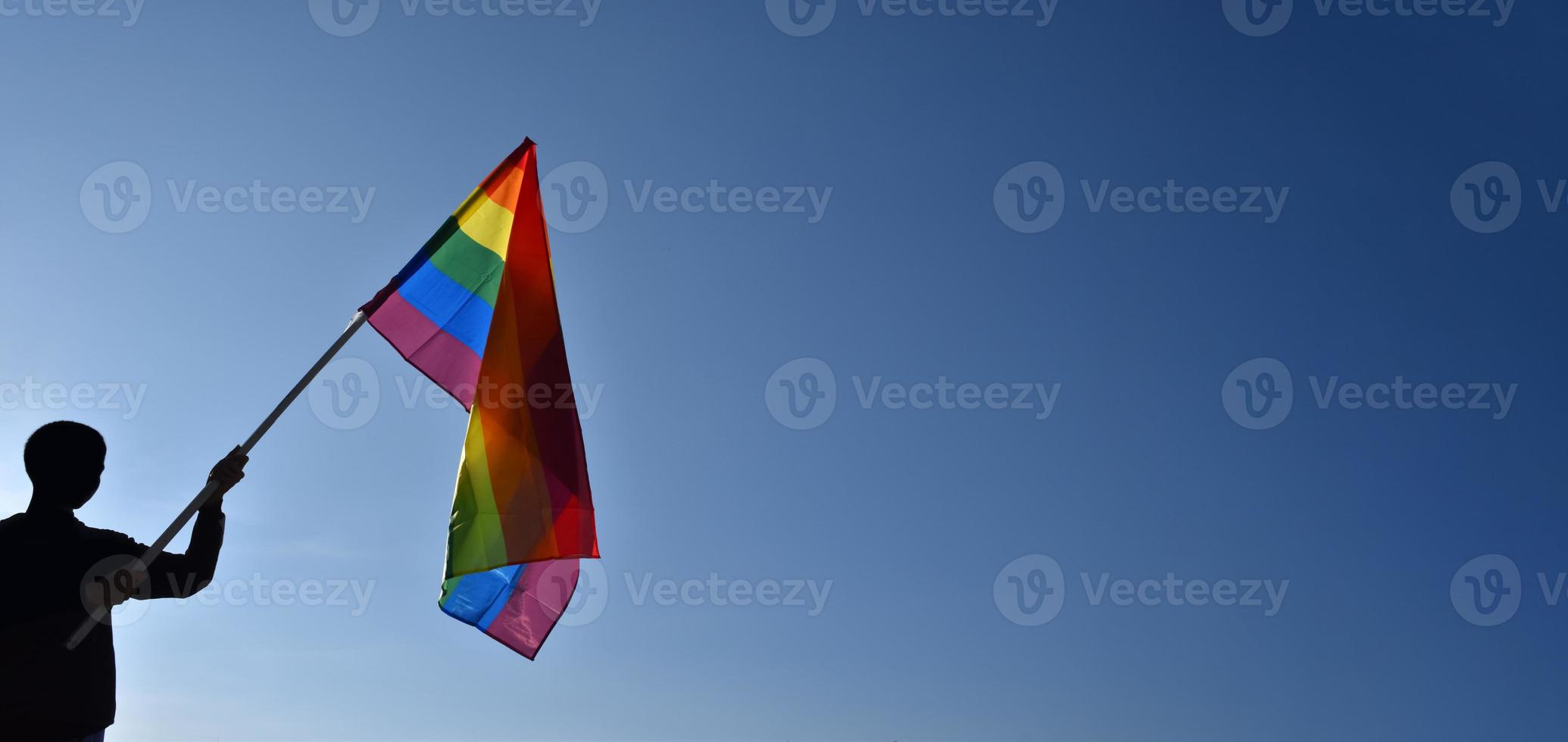 Rainbow flag holding in hand against bluesky background, concept for LGBT celebration in pride month, June, around the world. photo