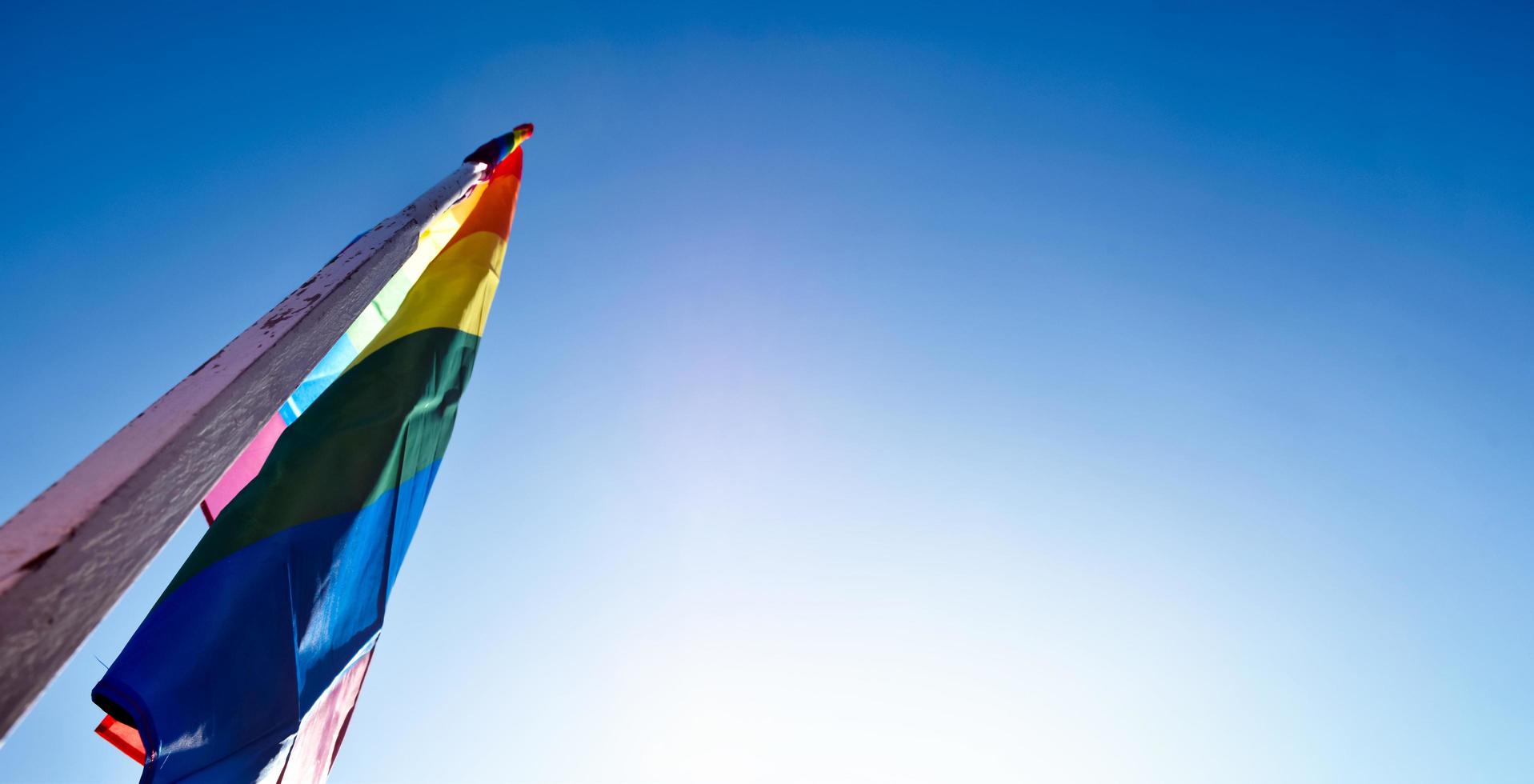 Look up view of rainbow flag, LGBT simbol, against clear bluesky background, soft and  selective focus, concept for LGBT celebration in pride month, June, around the world, copy space. photo