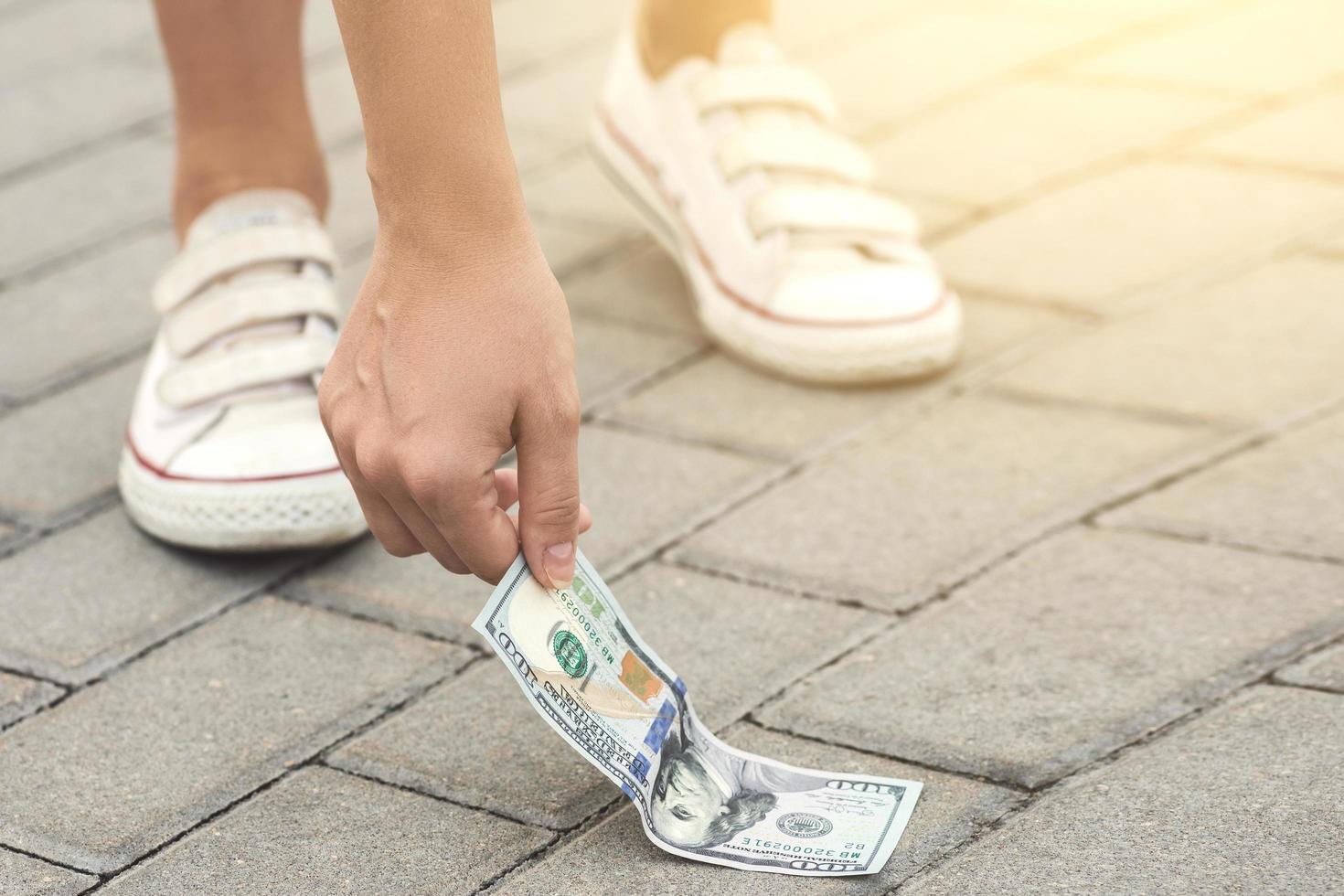 una mujer afortunada está recogiendo un billete de cien dólares del suelo. foto