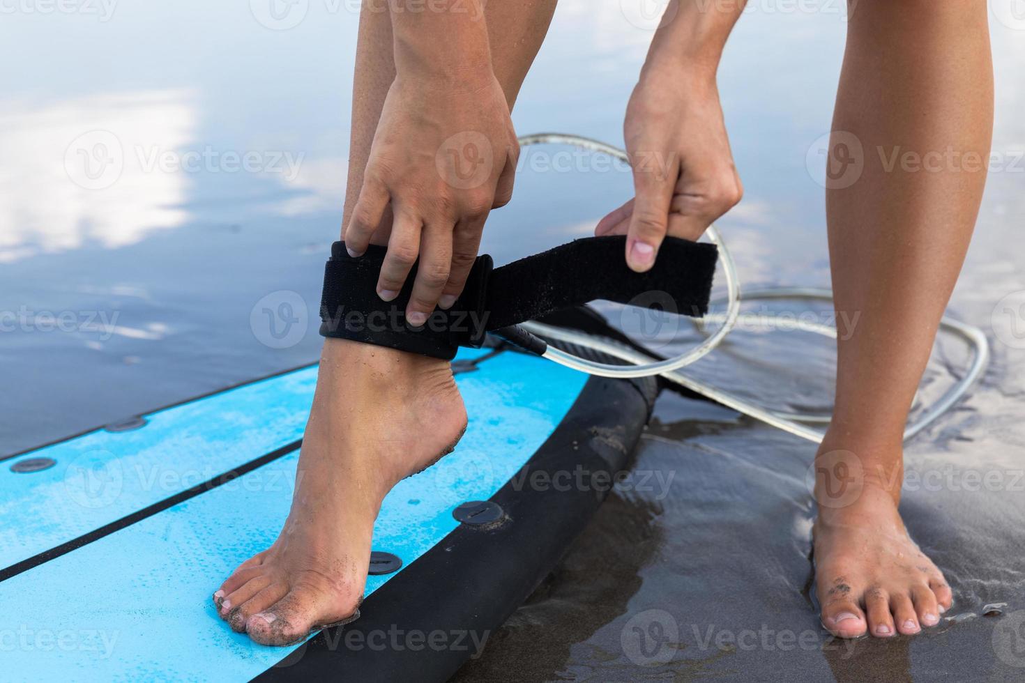 Woman is fastening surfing leash on her ankle photo