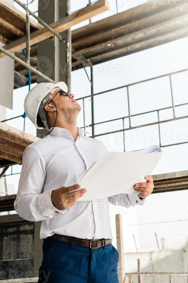 Man architect or businessman wearing hard hat and holding blueprints on a construction site photo
