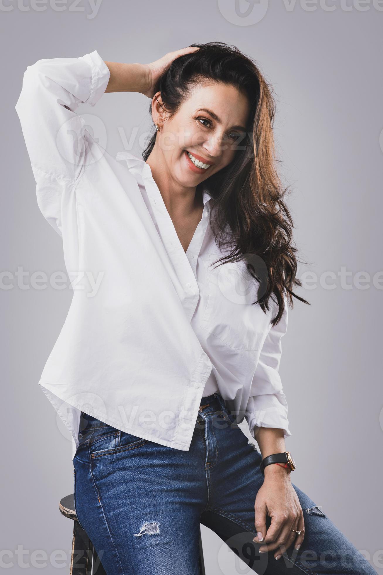 Beautiful middle aged woman wearing white shirt and jeans in photo
