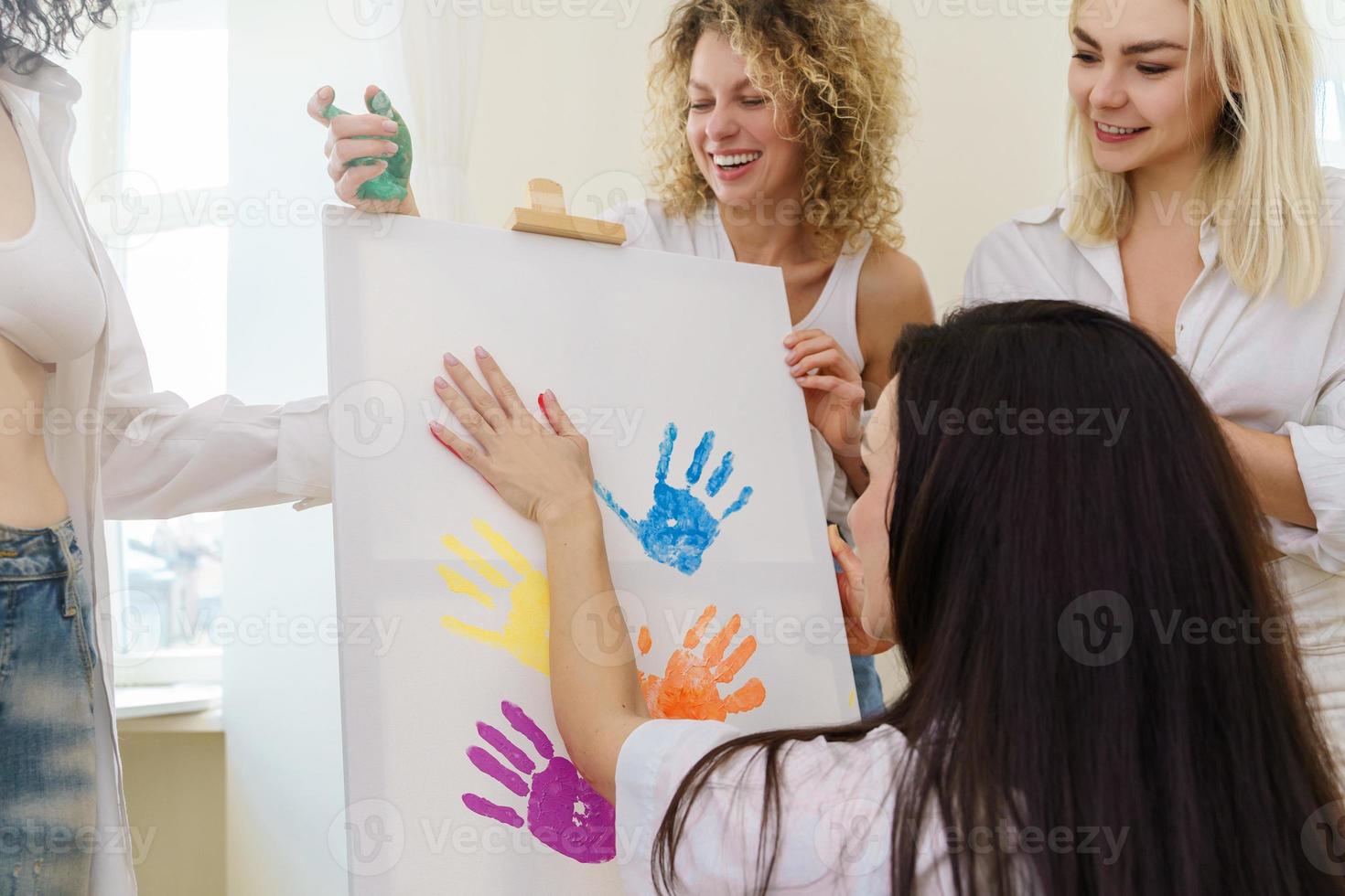 Group of women paint on canvas and drinking white wine during party at home photo