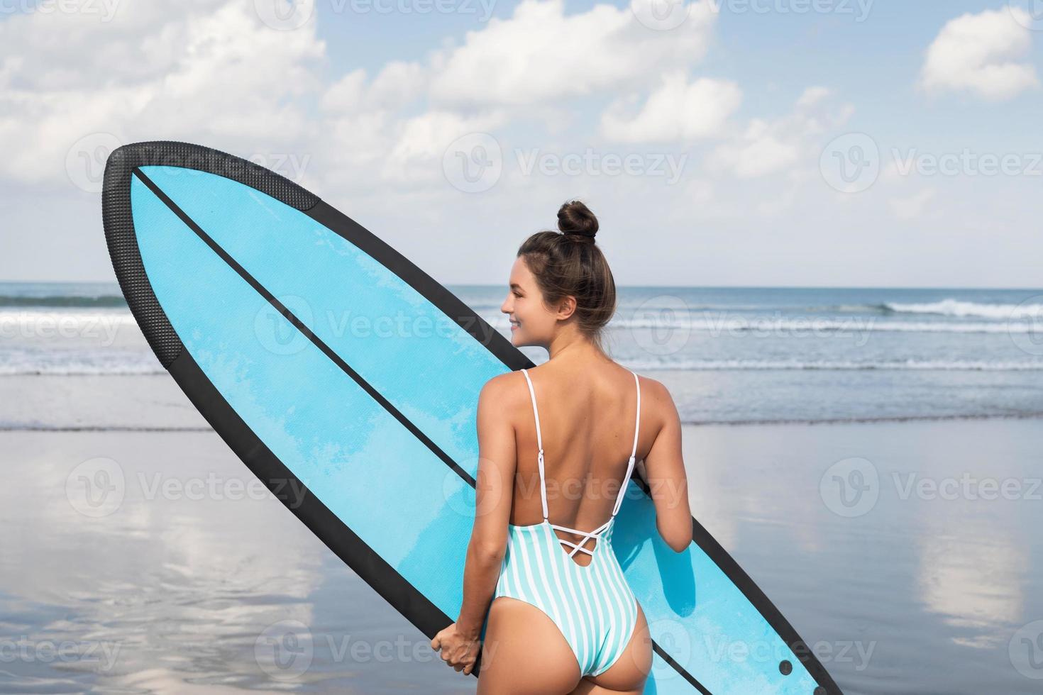 Young woman wearing striped swimsuit with surfboard on the beach photo