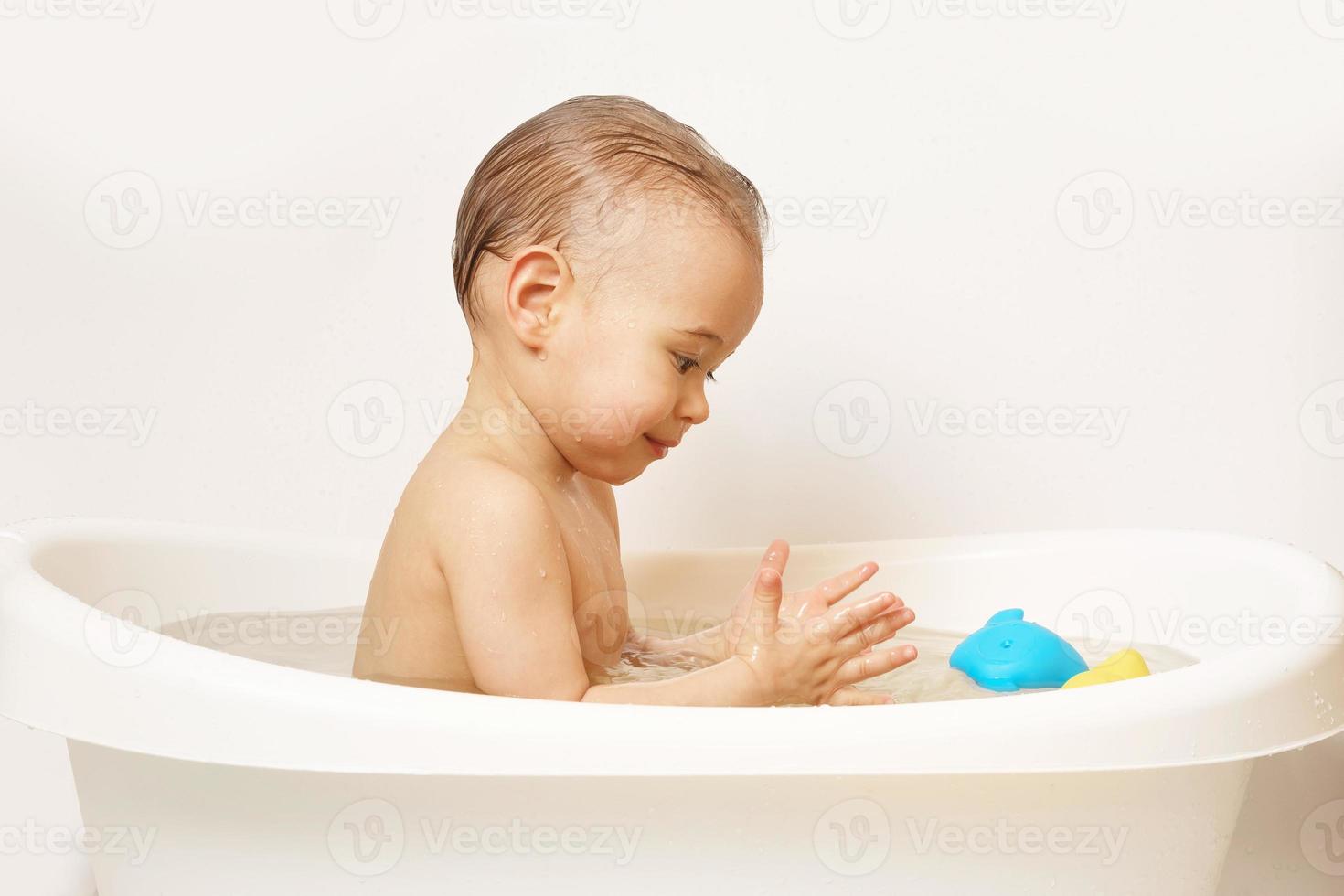 niño sonriente tomando un baño con juguetes de goma. foto