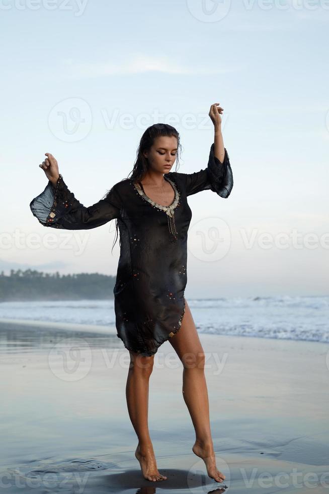 mujer sexy con túnica negra posa en la playa con arena negra foto