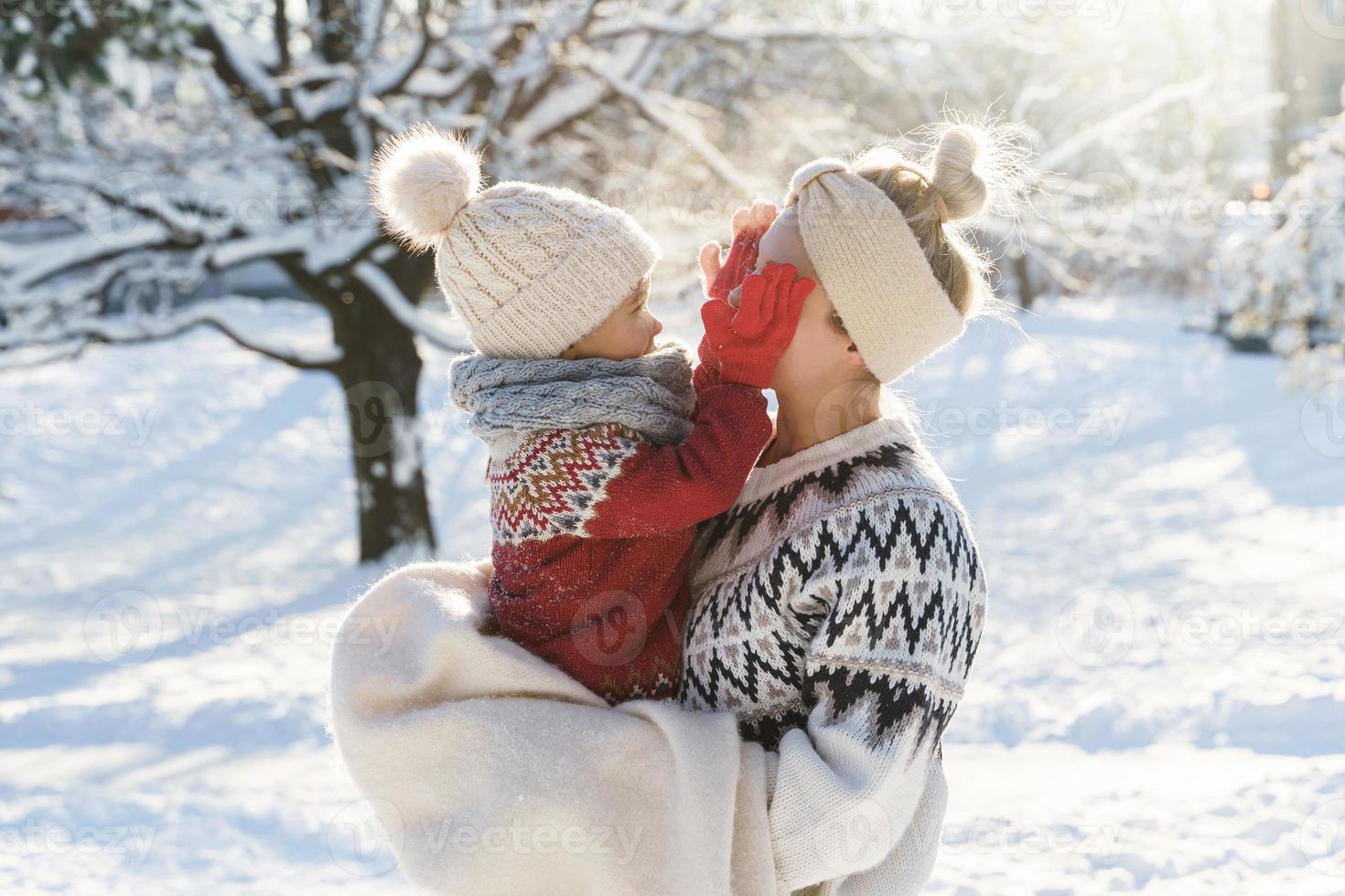 Young mother and her cute little son  playing peekaboo during sunny winter day photo